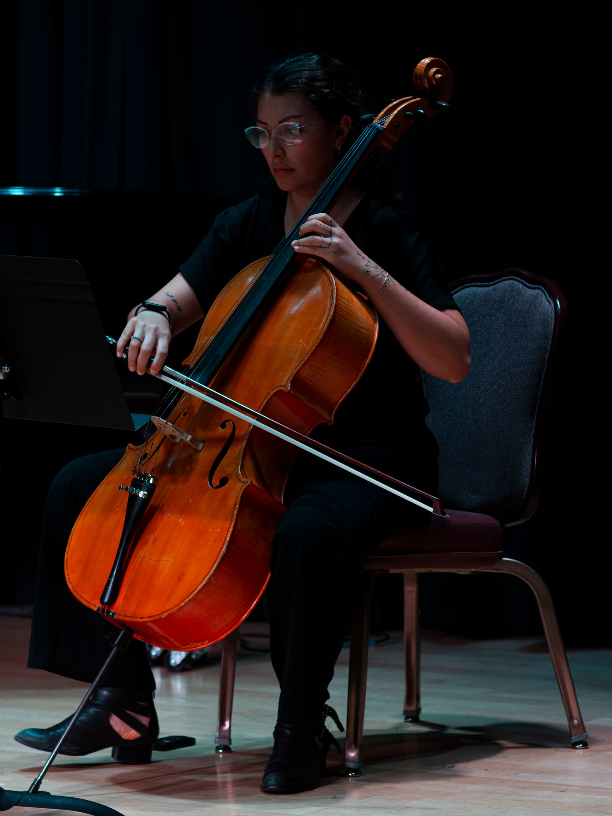 Dchenin playing the cello on a dark stage